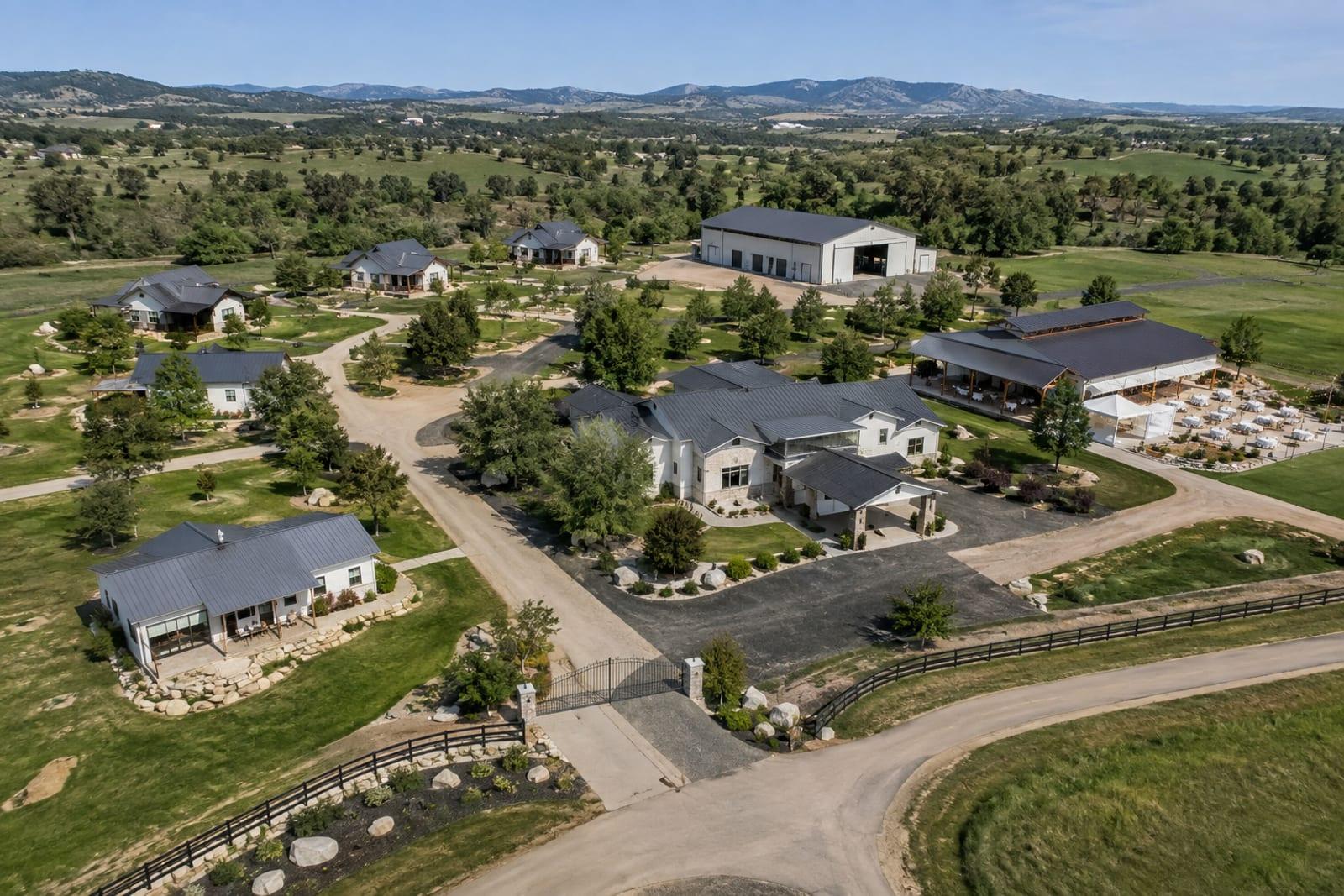 Aerial view of a multi-building estate with the office, event hall, cottages, barn and gate spread far apart across open land, none of them linked.